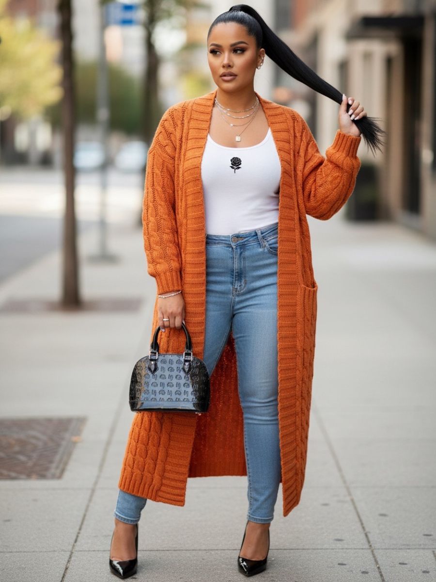 Li Amor woman model holding the black glossy Li Amor Rose, shell shape handbag. She's wearing an orange cardigan, white top, and blue jeans on a city street.